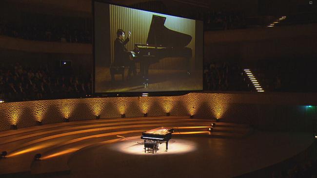 In der Elbphilharmonie bewegt ein unbesetzter Flügel die Tasten. Im Hintergrund ein Screen, auf dem man den Piansten Lang Lang an einem andern Ort und Flügel spielen sieht. 