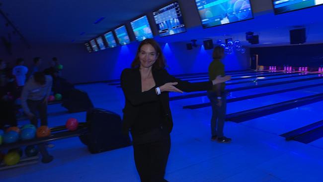 Eine junge Frau zeigt auf eine Bowlingbahn.