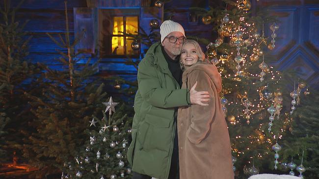 Ein mann mit Haube und ein junges Mädchen singen gemeinsam vor einem Weihnachtsbaum.