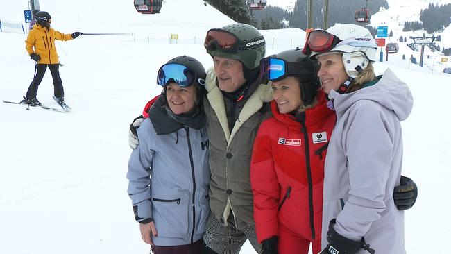 Vier Menschen stehen auf einer Skipiste und lächeln in eine Kamera