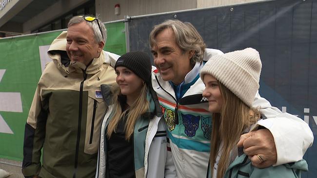 Ein älterer Mann in Skianzug posiert mit Fans für die Kamera.