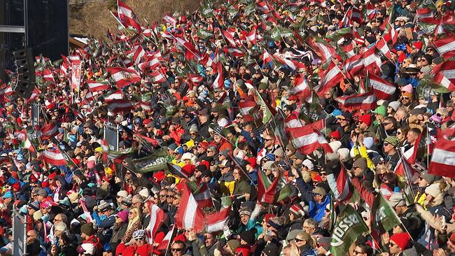 Auf einer Tribüne sitzen hunderte Menschen und schwenken Österreich-Fahnen.