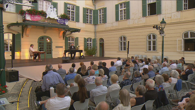 Joesi Prokopetz und Roman Grinberg sitzen auf der Bühne im Innenhof von Schloss Hunyadi 