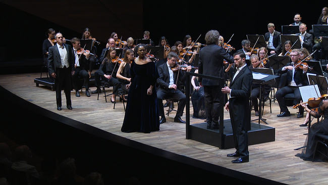 Opernsänger:innen und Orchester auf der Bühne