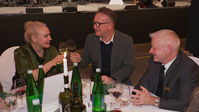 3 Menschen sitzen an einem runden Tisch und stoßen an