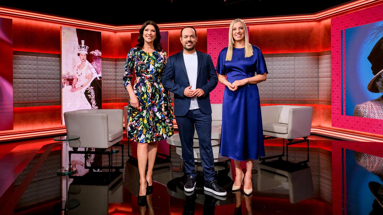  Marion Nachtwey, Patrick Budgen und Susanne Höggerl stehen in einem modern ausgeleuchteten TV‑Studio zwischen Sesseln und großen Porträtbildern von Queen Elizabeth II.