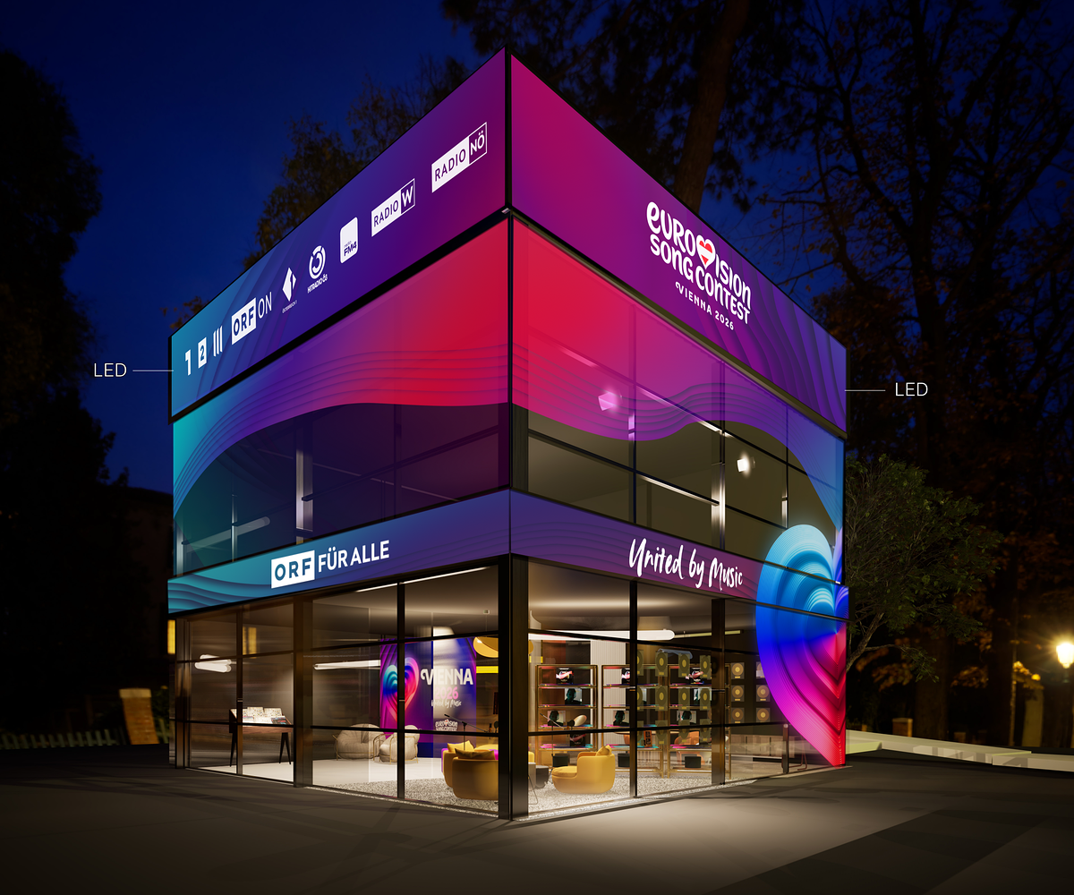 Das moderne ORF-Glasstudio in Kubusform am Rathausplatz ist nachts bunt beleuchtet und trägt ORF‑ und Eurovision‑Branding.