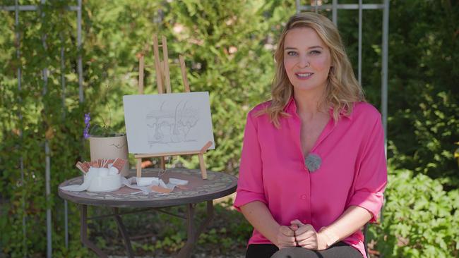 Christine Reiler in einer pinken Bluse sitzt in einem sonnigen Garten neben einem kleinen Tisch mit Staffelei, einem Bild zum Hautaufbau und Wundpflastern.