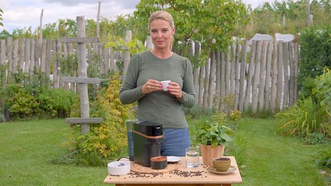 Christine Reiler steht im Garten neben einer Kaffeemaschine und hält eine kleine Espressotasse in den Händen.