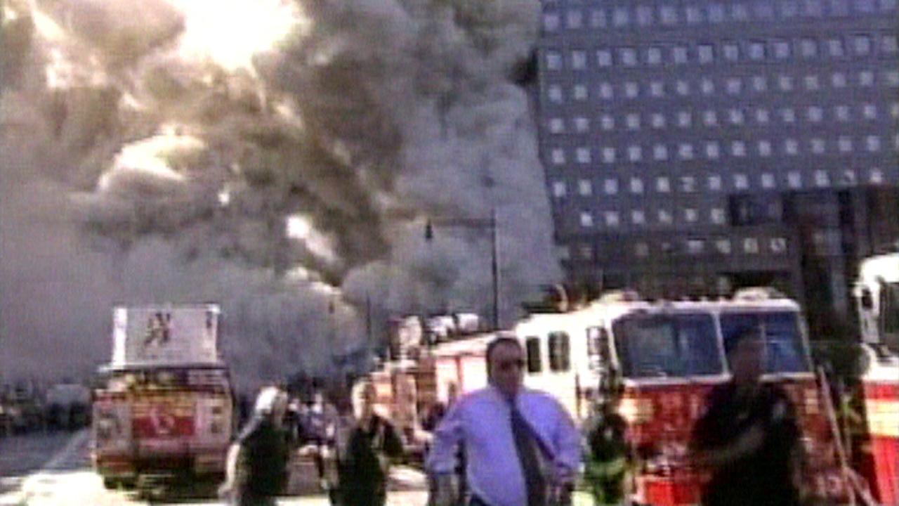 Anschlag auf das World Trade Center New York, das in Flammen steht, während Einsatzkräfte mit mehreren Feuerwehrfahrzeugen vor Ort sind.