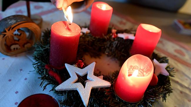 Eine Frau zündet am vierten Advent die vierte Kerze am Adventskranz an.