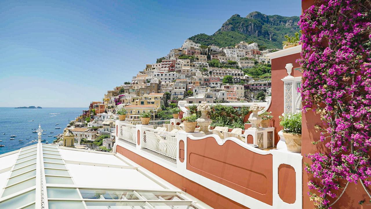 © ORF/Autentic GMBH Blick von einer blumengeschmückten Terrasse auf die dicht gebaute Küstenstadt Positano an der italienischen Amalfiküste mit der Insel Capri im Hintergrund