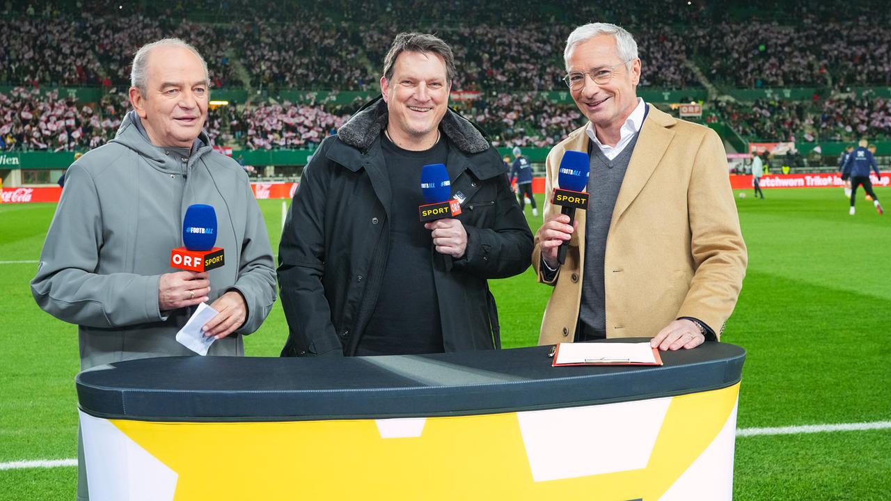 Herbert Prohaska, Andreas Herzog und Rainer Pariasek stehen mit ORF-Sport-Mikros hinter dem Moderatorenpult vor dem Fußballfeld in einem voll besetzten Fußballstadion.