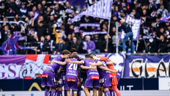 Das Team von FK Austria Wien in violetten Trikots steht im Kreis vor einer dicht gefüllten Fankurve im Rahmen der Admiral Bundesliga-Begegnung zwischen FK Austria Wien und LASK in Wien. 
