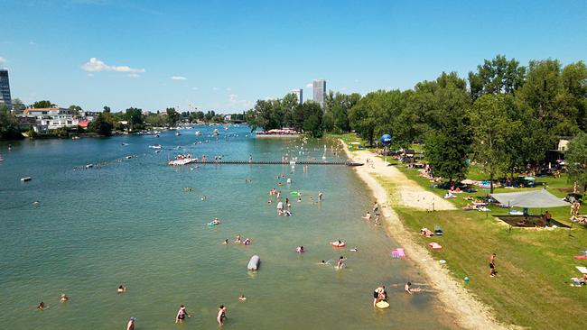 Das Bild zeigt zahlreiche Menschen beim Baden und Entspannen an der Alten Donau an einem sonnigen Tag in der Stadt.