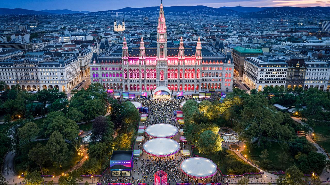 © ZOOMVP/Stadt Wien Marketing Das Wiener Rathaus ist bei Abenddämmerung festlich beleuchtet, davor füllt ein großes Event das Parkgelände.