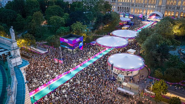 Eine lange, beleuchtete Event‑Promenade mit türkisem Teppich und Pavillions zieht sich durch den Park, dicht umgeben von Besuchern.