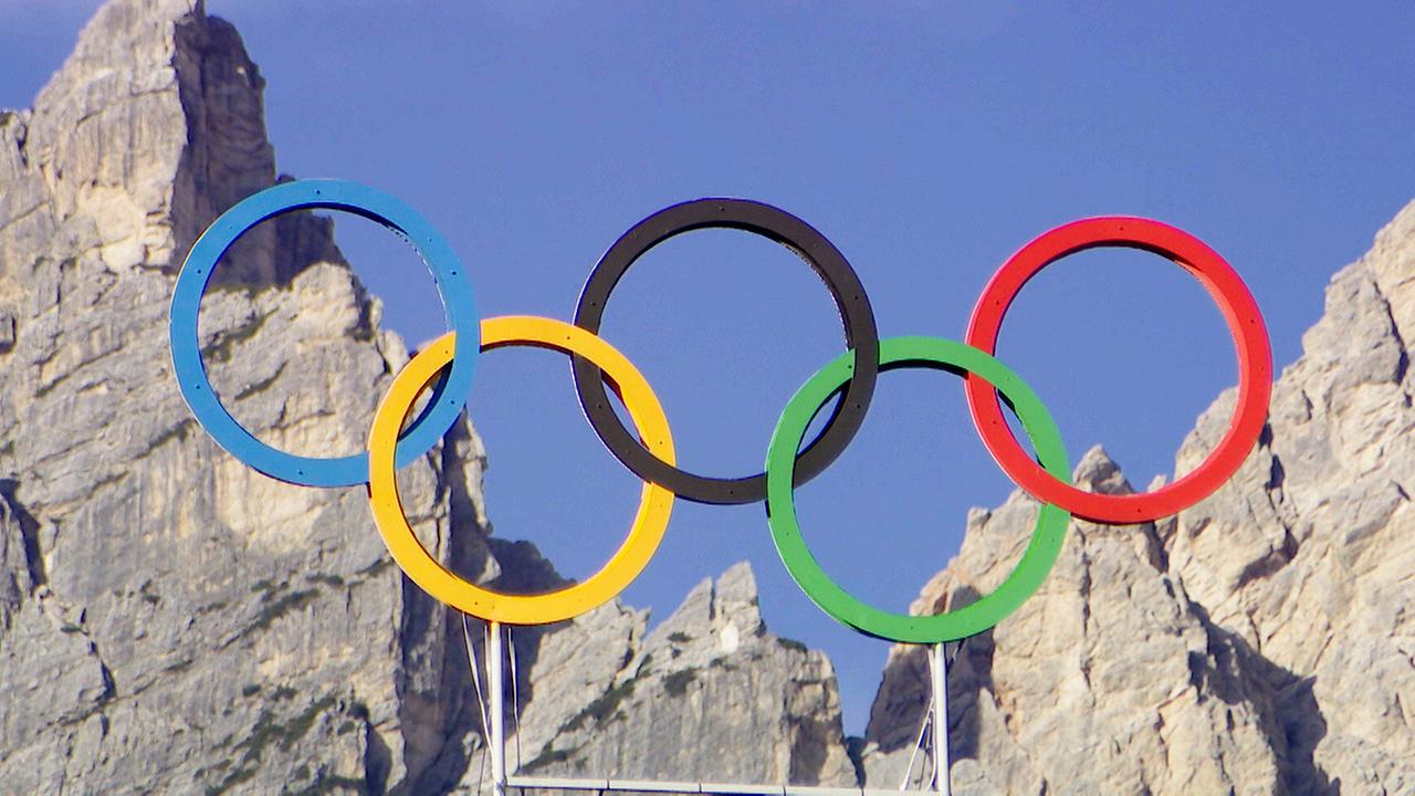 © ORF/ORF-Tirol Olympische Ringe vor den Dolomiten über Cortina bei Sonnenschein und blauem Himmel