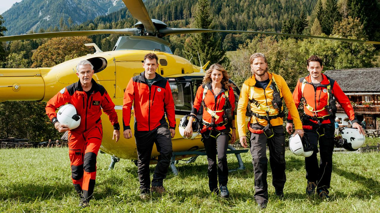 © ORF/ZDF/Sabine Finger "Die Bergretter" Robert Lohr, Michael Pascher, Luise Bähr, Sebastian Ströbel und Markus Brandl vor einem Helikopter auf einer Bergwiese
