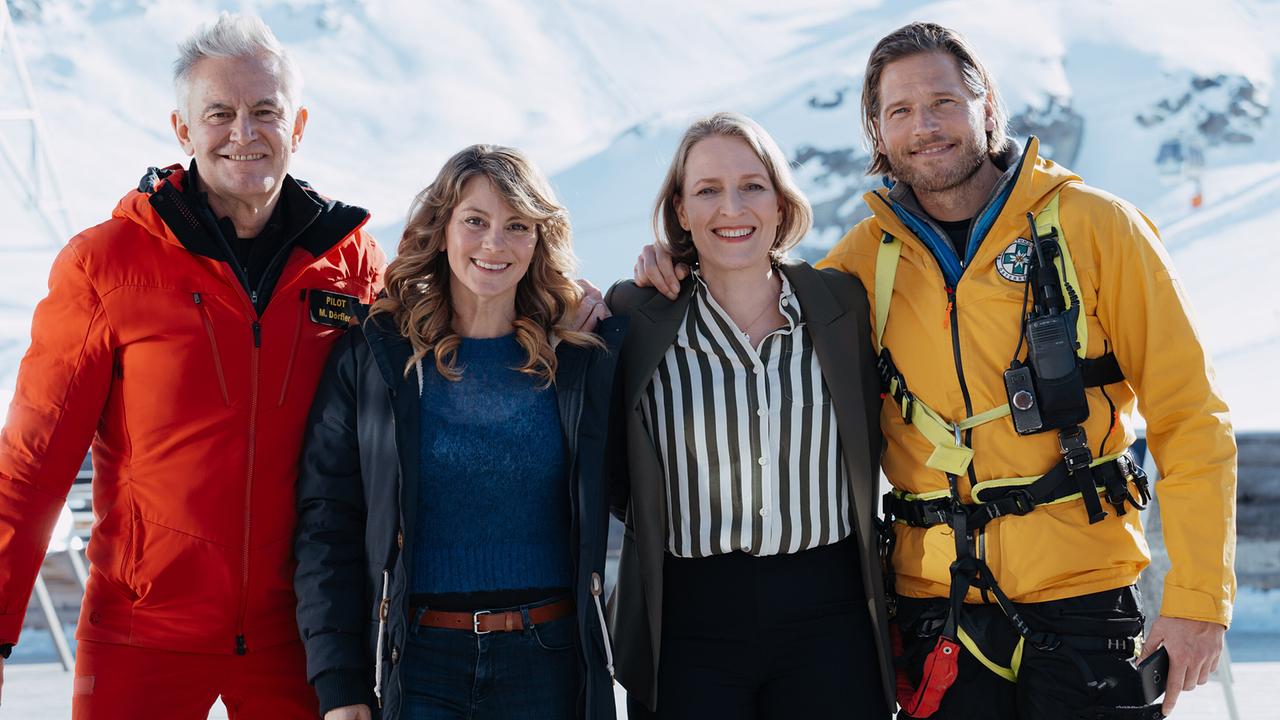 © ORF/ZDF/Sabine Finger Ein starkes Team: Pilot Michi (Robert Lohr, l.), Katharina (Luise Bähr, 2. v. l.), Emilie (Stefanie von Poser, 2. v. r.) und Bergretter Markus (Sebastian Ströbel, r.) posieren lächelnd vor einer verschneiten Bergkulisse.