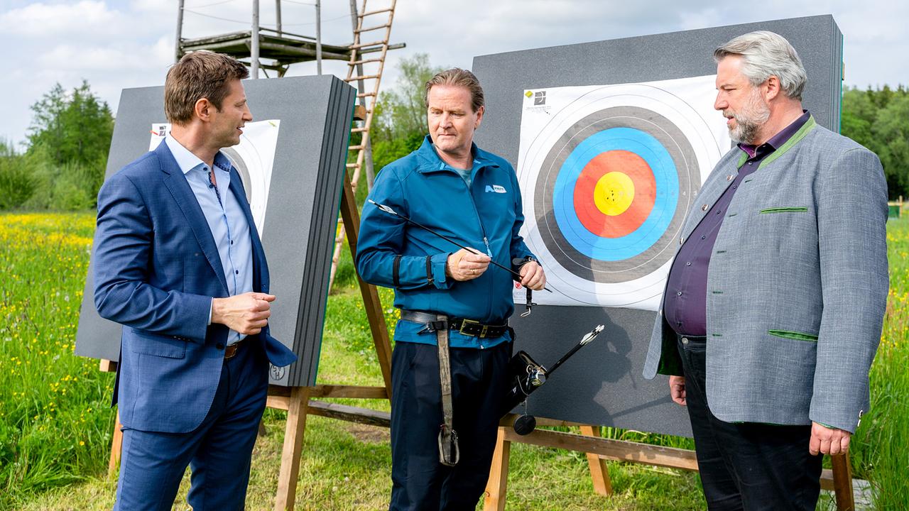 Die Kommissare Hansen und Stadler erkundigen sich auf einem Bogenschießplatz vor Zielscheiben beim Bogenschützen Walter Hofmeister, ob er mit Jagdpfeilspitzen schießt.