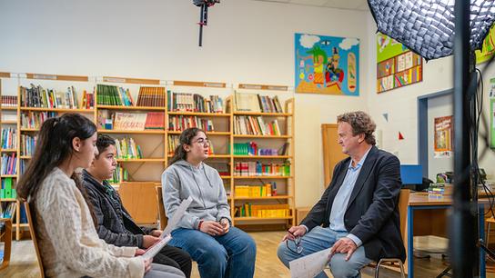 Hanno Settele spricht mit Schüler und Schülerinnen in einem Klassenraum an einer Mittelschule in Wien.