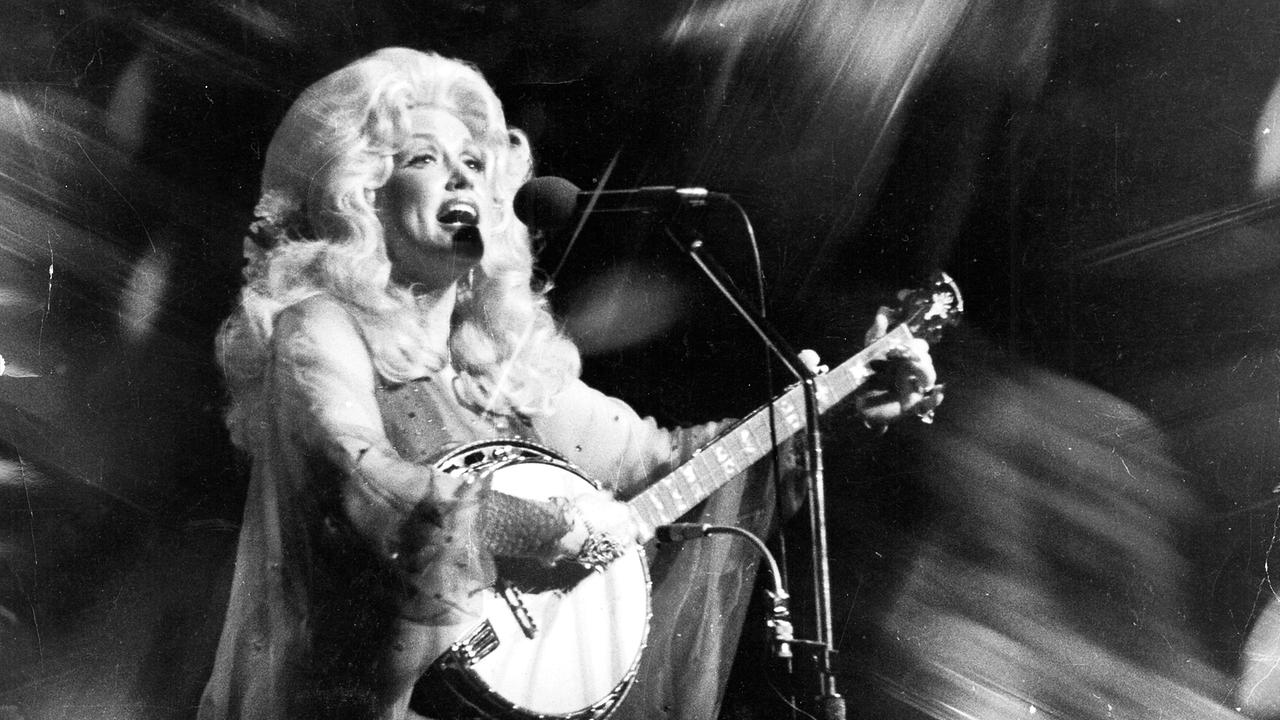 Dolly Parton singt auf einer Bühne in ein Mikrofon und spielt dabei Banjo, fotografiert in den 1970er Jahren