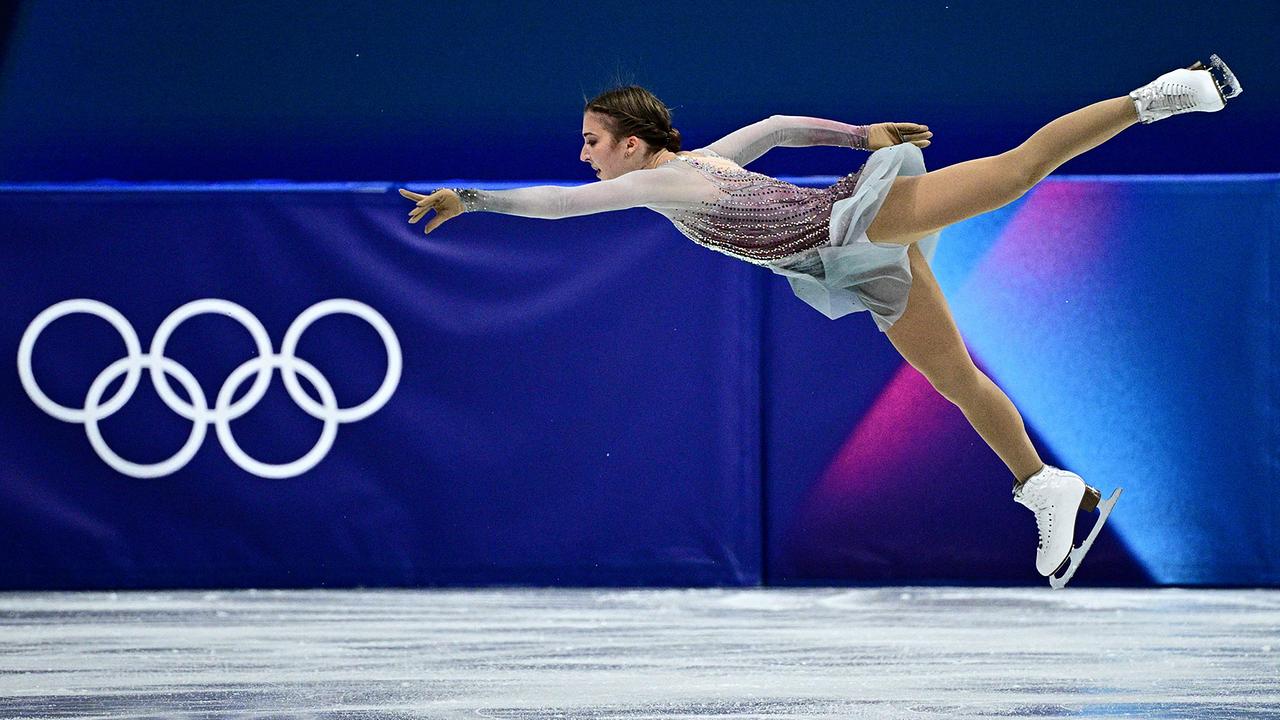 Die Österreicherin Olga Mikutina zeigt bei den Olympischen Spielen eine Flugfigur über dem Eis, im Hintergrund sind die olympischen Ringe zu sehen - beim Kurzprogramm im Eiskunstlauf der Damen bei den Olympischen Winterspielen Milano Cortina 2026.