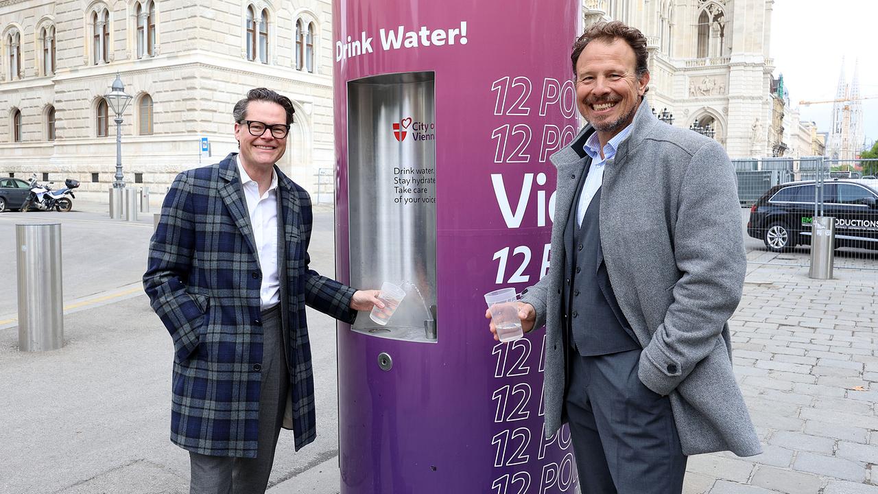 Vienna’s City Councillor for Climate Action, Jürgen Czernohorszky and Michael Krön, Executive Producer of the ESC stand outdoors by a public drinking water fountain, each holding a cup of water in front of a historic building.