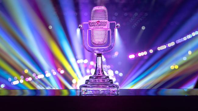 Die ESC 2026 Trophy in Mikrofonform steht vor einer Bühne mit bunten Lichtstrahlen und trägt das Logo des Eurovision Song Contest.