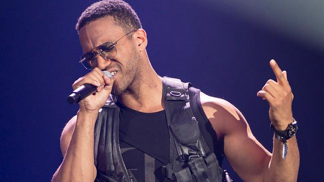 © ORF/Thomas Jantzen Cesár Sampson singt auf einer Bühne, hält ein Mikrofon und trägt ein schwarzes Outfit mit einem auffallenden Ledergilet.