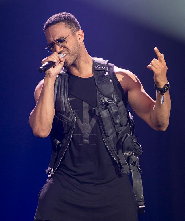Cesár Sampson singt auf einer Bühne, hält ein Mikrofon und trägt ein schwarzes Outfit mit einem auffallenden Ledergilet.