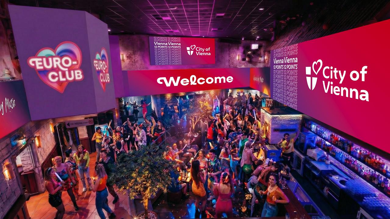 © ZOOMVP/Stadt Wien Marketing Im Euro‑Club tanzen und feiern viele Menschen in farbigem Licht vor Bars und ESC‑Dekorationen.
