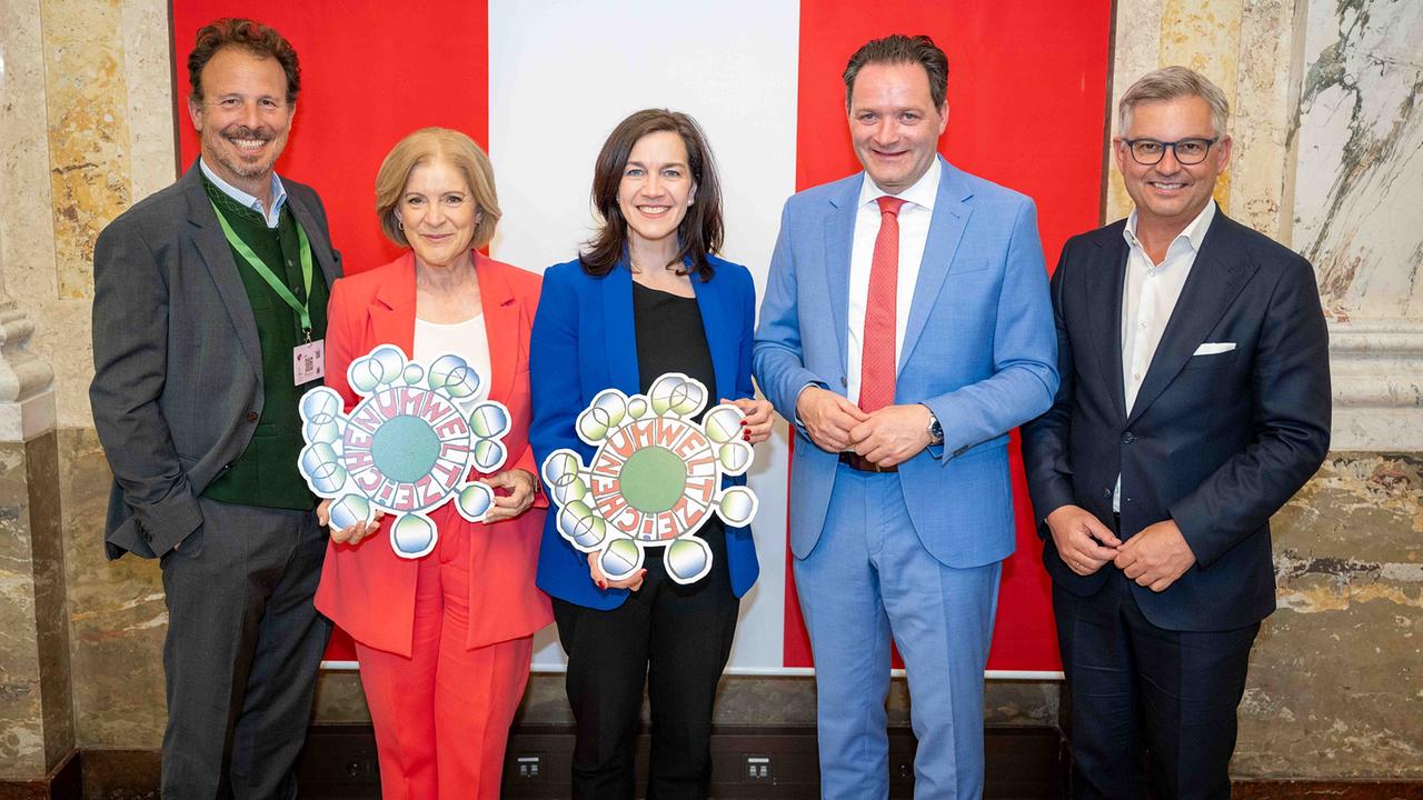 © ORF/BMLUK/Rene Hemerka Group photo with Michael Krön (ESC Executive Producer ORF), ORF Director General Ingrid Thurnher, Anita Malli, Federal Minister Norbert Totschnig, Magnus Brunner in a representative room in front of a red-white-red backdrop, symbolically holding the environmental symbol in their hands.