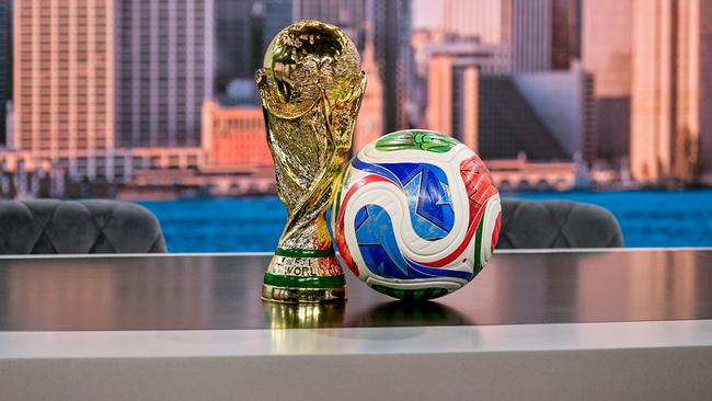 Der Fußball‑WM‑Pokal steht neben einem bunten Spielball auf einem Tisch vor einer urbanen Skyline‑Kulisse im neuen ORF WM-Studio