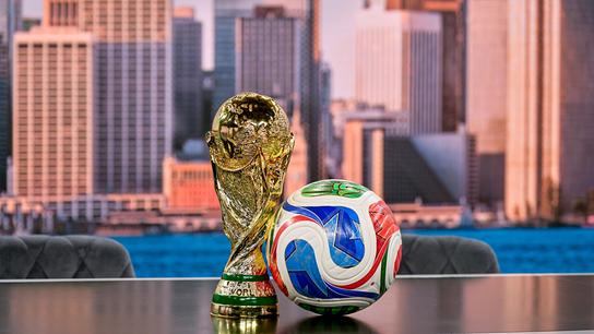 © ORF/Thomas Ramstorfer Der Fußball‑WM‑Pokal steht neben einem bunten Spielball auf einem Tisch vor einer urbanen Skyline‑Kulisse im neuen ORF WM-Studio