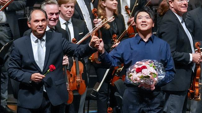 © ORF/Roman Zach-Kiesling Dirigent Tugan Sokhiev und Pianist Lang Lang mit einem Blumenstrauß in der Hand stehen vor den Wiener Philharmonikern Hand in Hand auf der Bühne.