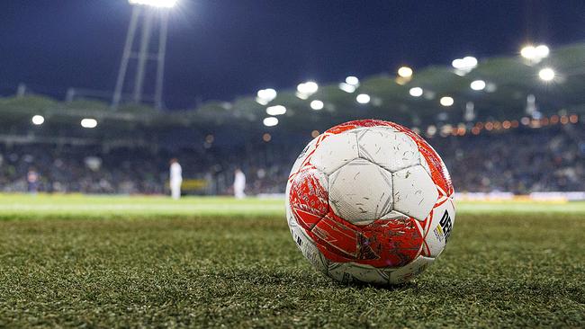 Ein rot-weiß-roter Fußball der Bundesliga liegt in der Nacht im Stadion am Rasen und im Hintergrund brennt das Flutlicht.