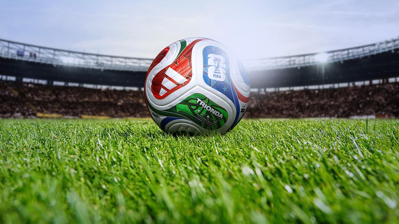 © ORF Der Fußball-WM-Ball liegt auf dem Rasen eines voll besetzten Stadions.