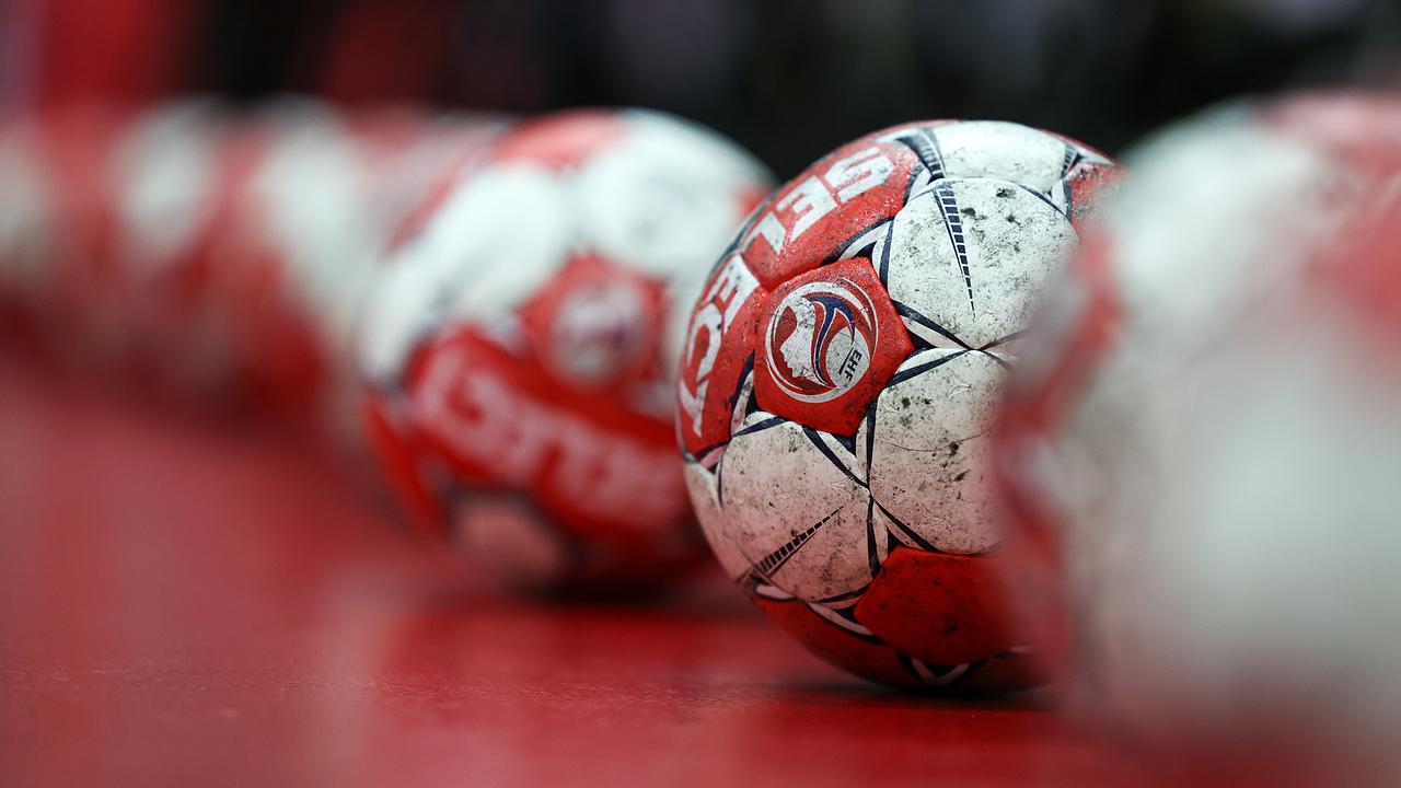 Mehrere rot-weiße Handbälle liegen in einer Reihe auf einem roten Boden.