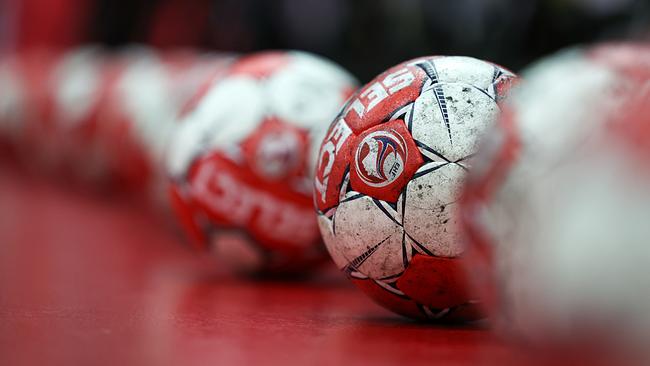 Mehrere rot-weiße Handbälle liegen in einer Reihe auf einem roten Boden.