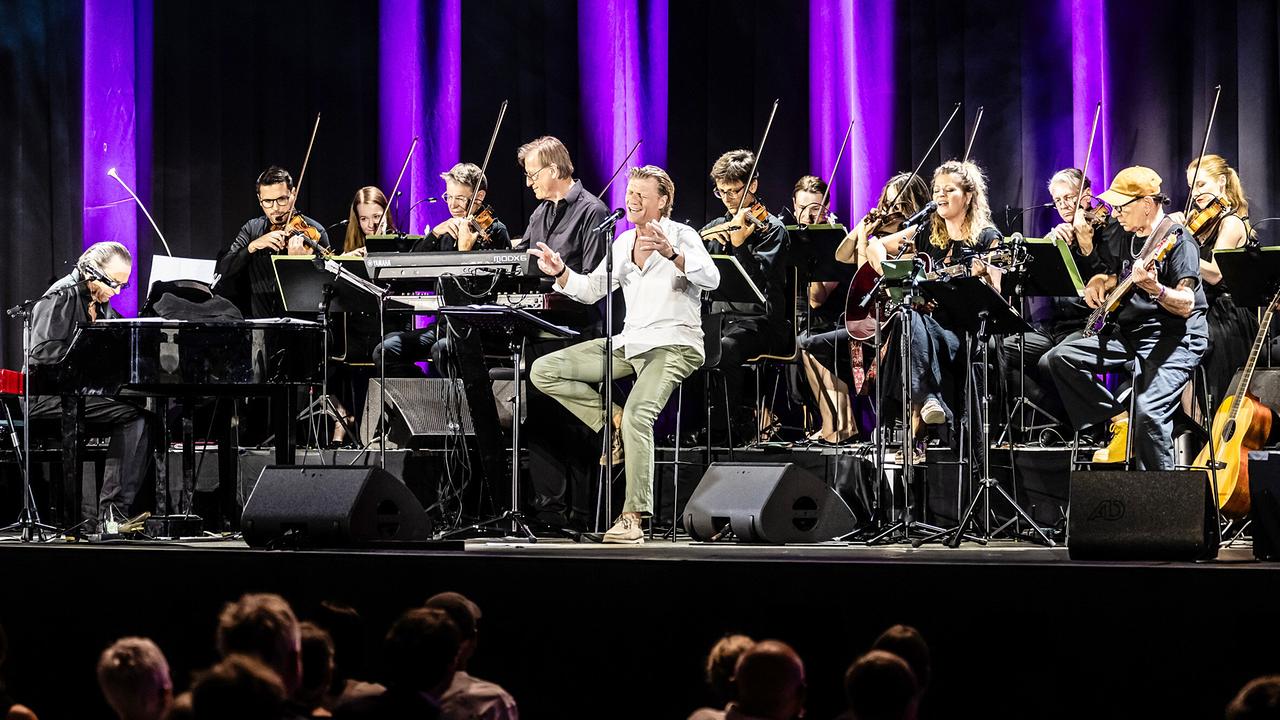Gery Seidl tritt gemeinsam mit Christian Kolonovits und den Wiener Symphonikern auf einer violett ausgeleuchteten Open-Air-Bühne im Wiener „Theater im Park“ auf.