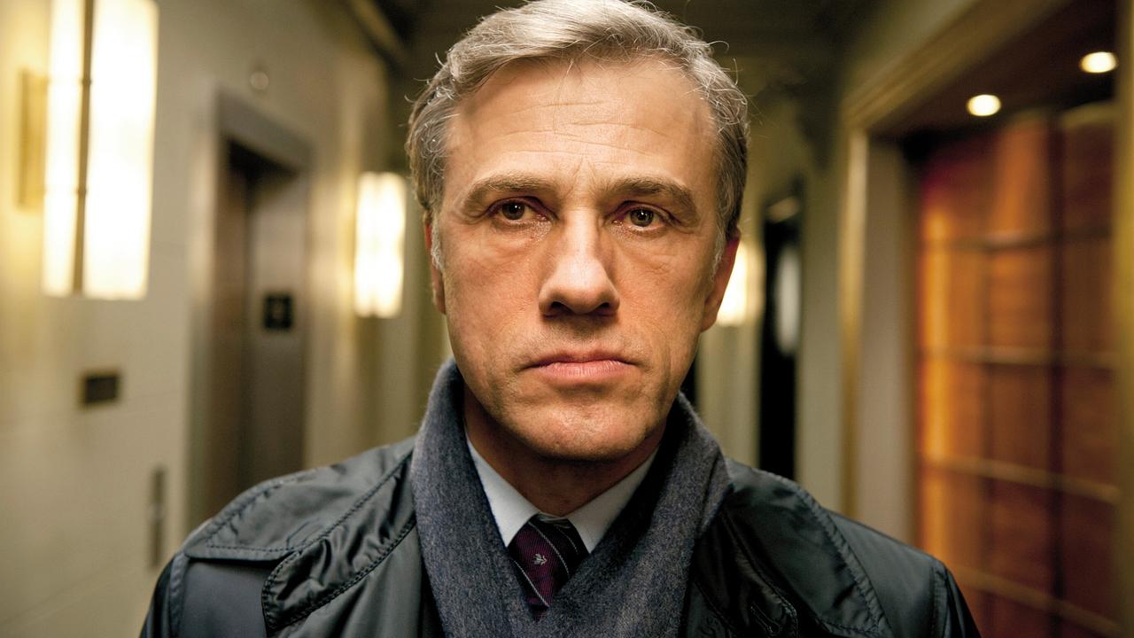 © ORF/Constantin Film Christoph Waltz als Alan Cowan steht in einem warm beleuchteten Hotelflur und schaut direkt in die Kamera in "Gott des Gemetzels"