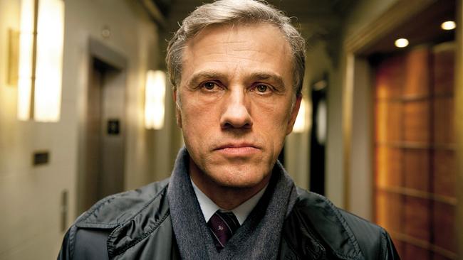 © ORF/Constantin Film Christoph Waltz als Alan Cowan steht in einem warm beleuchteten Hotelflur und schaut direkt in die Kamera in "Gott des Gemetzels"