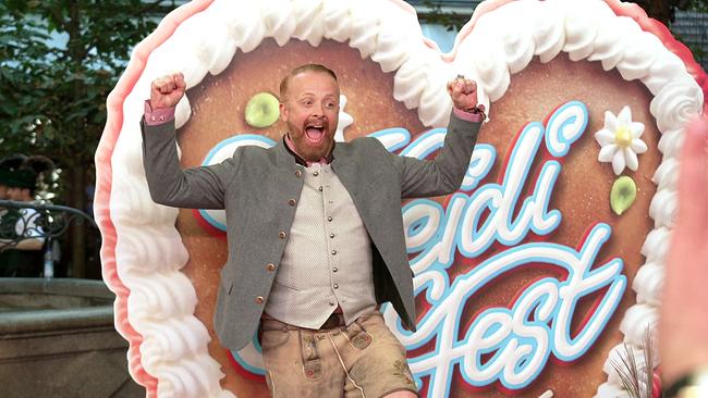 Ross Anthony in Tracht steht jubelnd  vor einer überdimensionalen, mit Sahne verzierten Herztorte beim Heidifest in München.