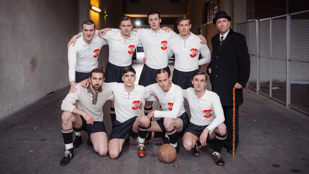 © ORF/Rizar.Photo/Gabriel Alarcon Das Wunderteam in historischen Fußballtrikots mit Trainer Hugo Meisl im Mantel mit Hut und Gehstock posiert im Stadion Gang (Praterstadion).