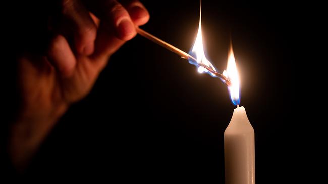 Eine Kerze wird mit einem brennenden Streichholz angezündet.