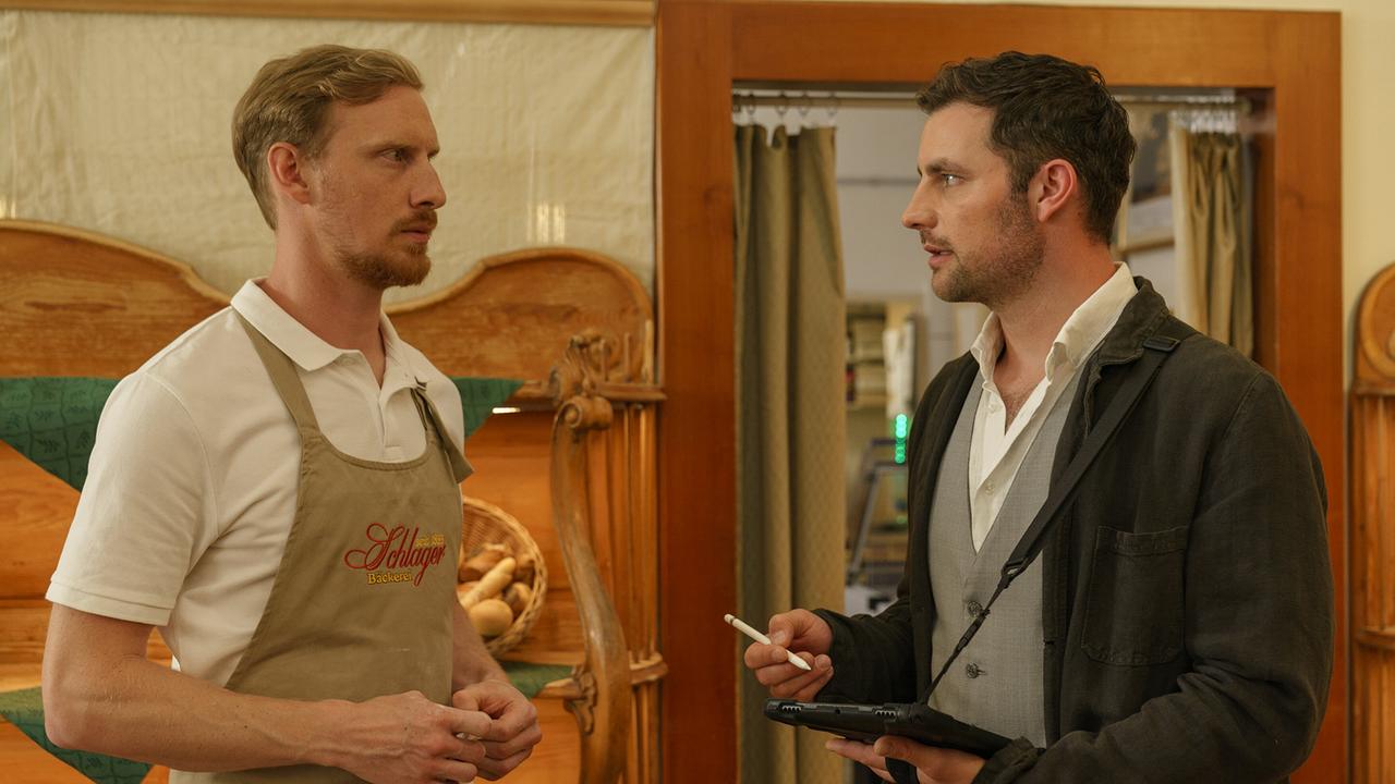 Inspektor Felix Burger befragt Christian Schilling von der Bäckerei Schlager in einem rustikalen Ladenraum.