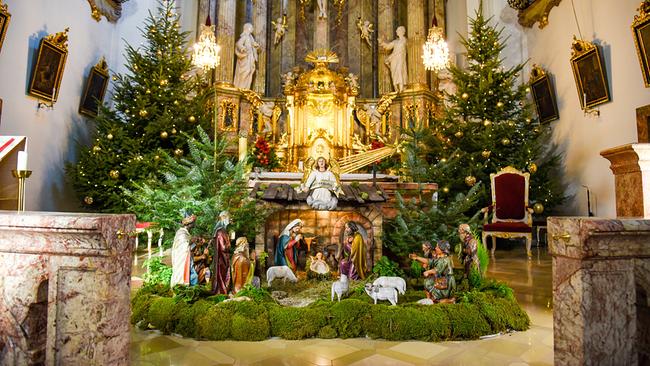 Weihnachtskrippe mit Figuren in der weihnchtlich geschmückten Franziskanerkirche mit Weihnachtsbäumen vor dem Altar in St. Pölten