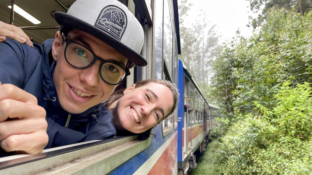 © ORF/Tambalina Entertainment Melanie Flicker und Christoph Hirschler lehnen sich lächelnd während der Fahrt aus dem Fenster eines Zuges, der durch dichtes Grün fährt.